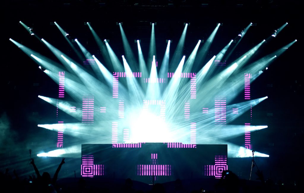 Escenario de gran evento con luces blancas y pantallas LED rosas en formación simétrica sobre fondo negro