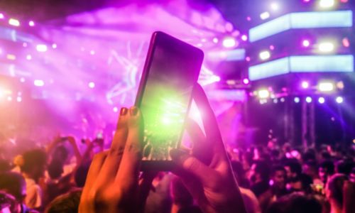 Mano sosteniendo un móvil grabando un festival con luces rosas y moradas y multitud al fondo